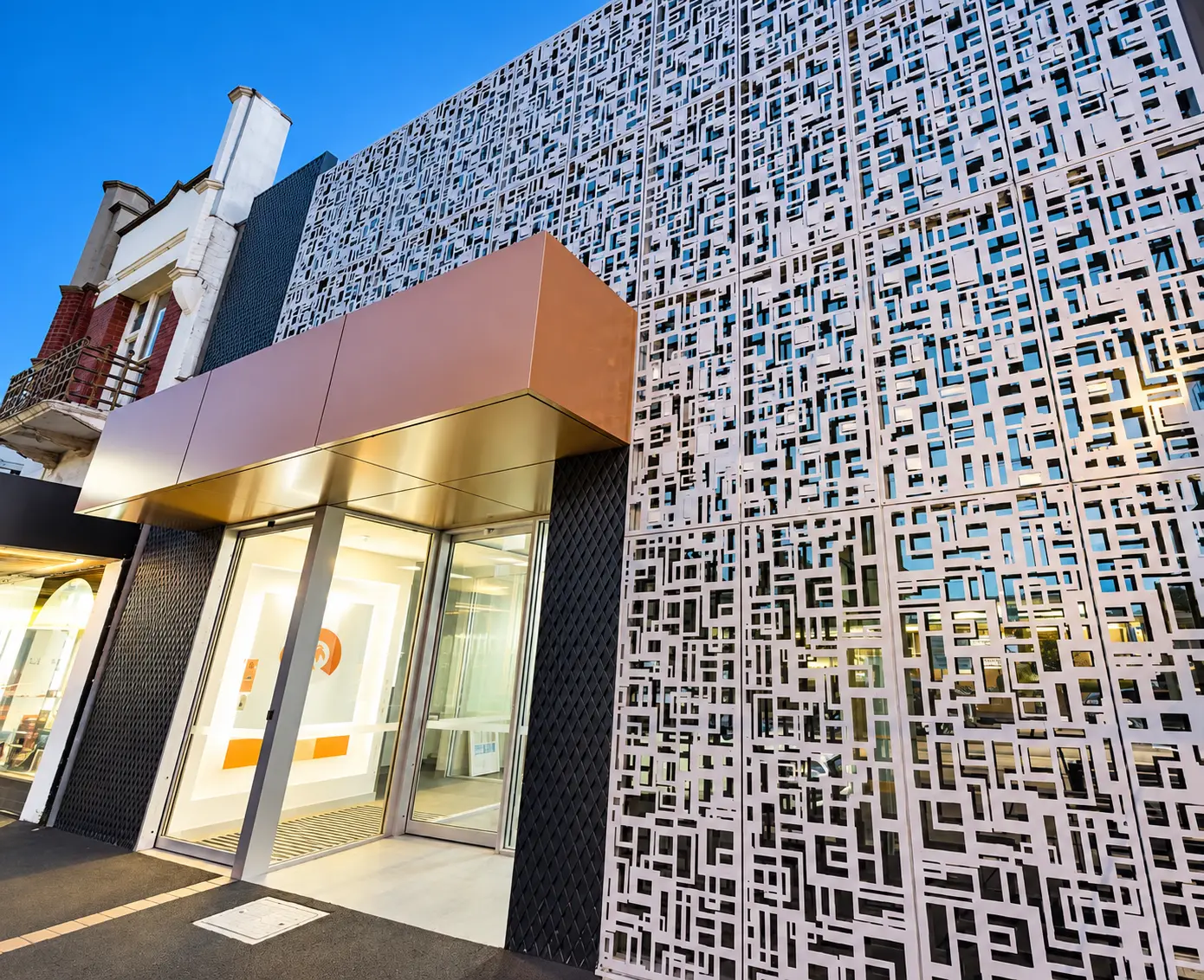 Perforated metal building façade with a warm metallic entrance canopy